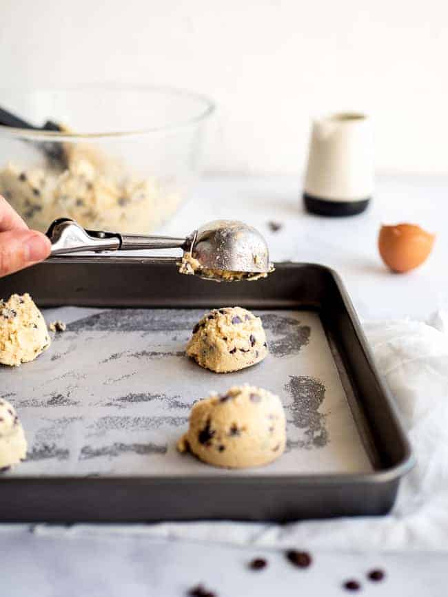 hand holding icecream scoop with chocolate chip cookies on a baking sheet